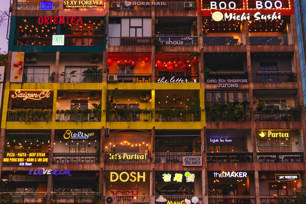 An apartment building in Ho Chi Minh City with lit signs of cafe names at night.