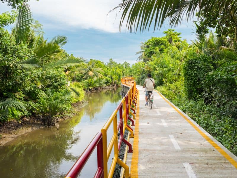 A person biking on the road by the river in Bangkok, Thailand.
