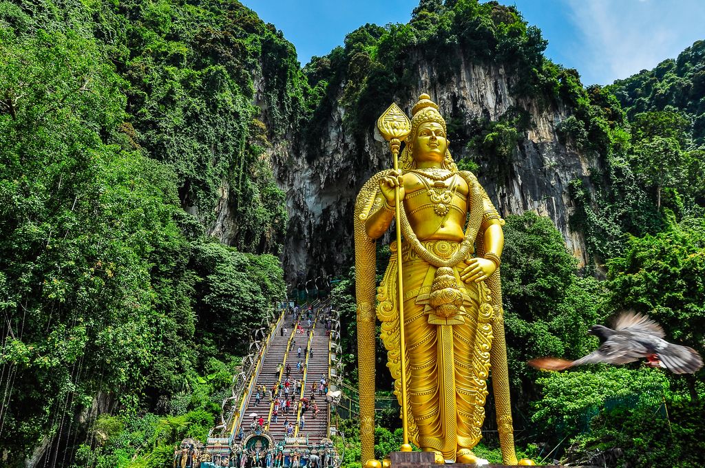 A giant golden statue of a Hindu god and the colorful stairs at the entrance of Batu Caves, Malaysia.