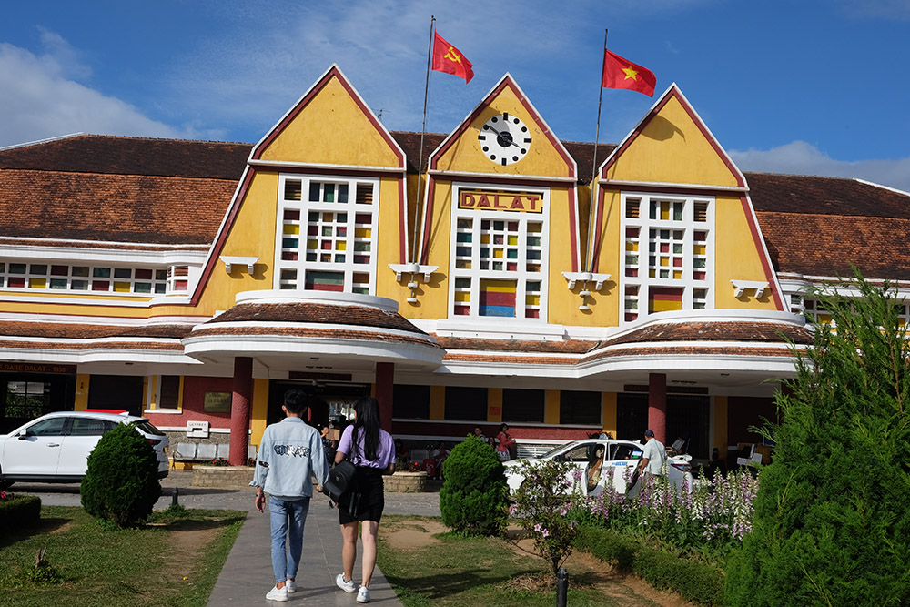 Two people walking to a yellow train station building in Dalat, Vietnam.
