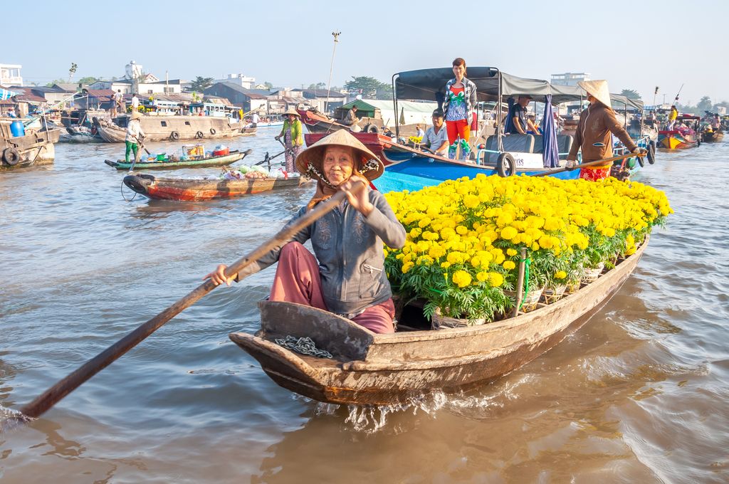 An old woman rowing on a boat full of yellow flowers on a floating market in Mekong Delta, South Vietnam.