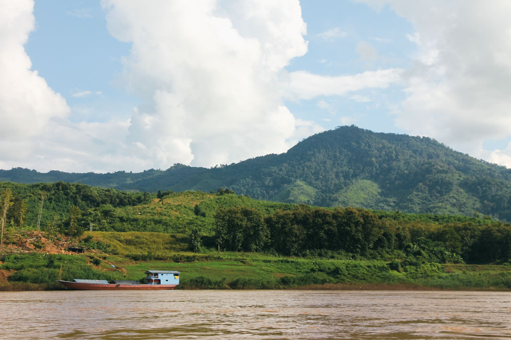 A river with a boat and hills in the background on a sunny day in Laos.