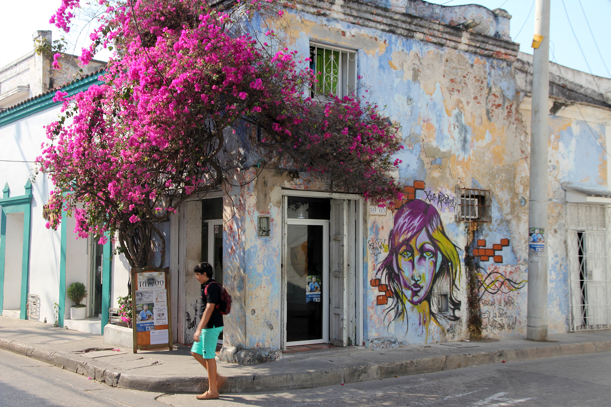 A corner of a building with flowers and wall art, a man passing by