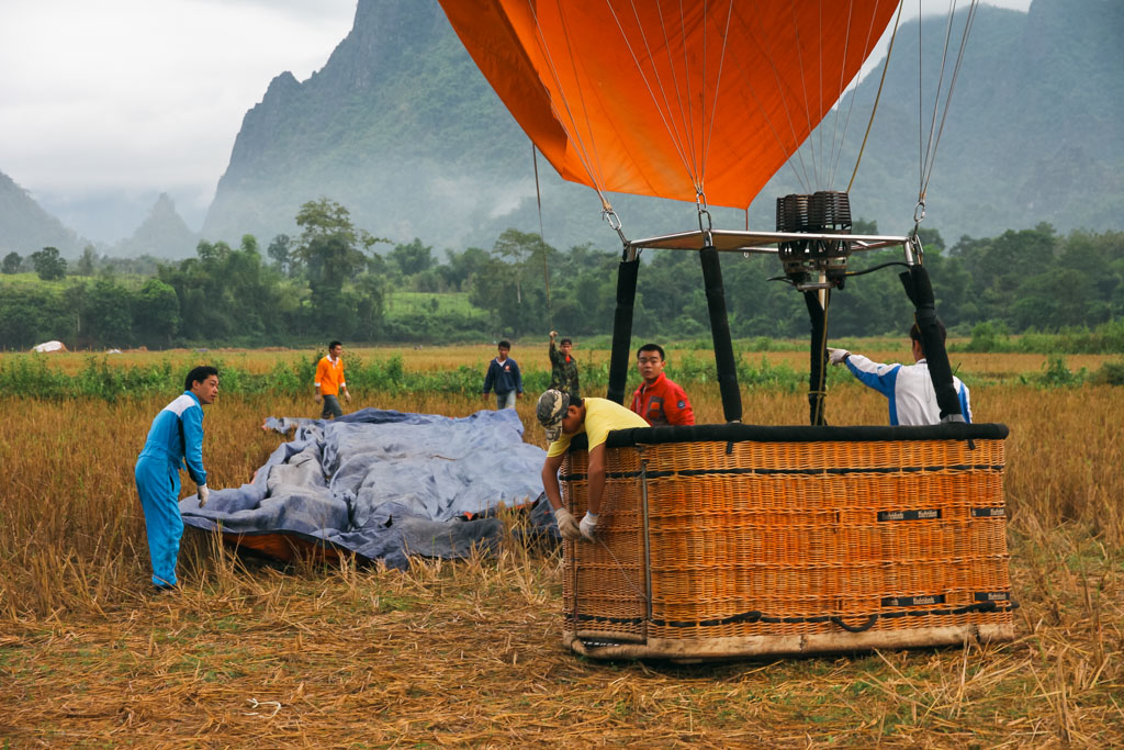 Seven men setting up a hot air balloon in a town surrounded by mountains in Vang Vieng, Laos.
