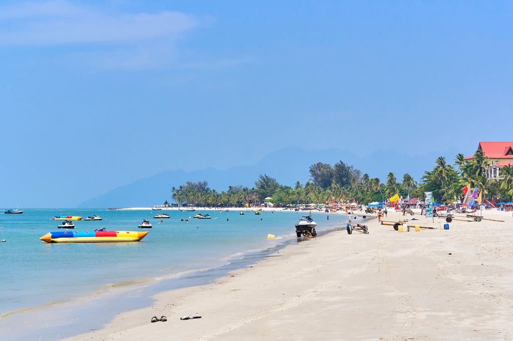 Blue sea waters and a crowded white sand beach in Langkawi, Malaysia.