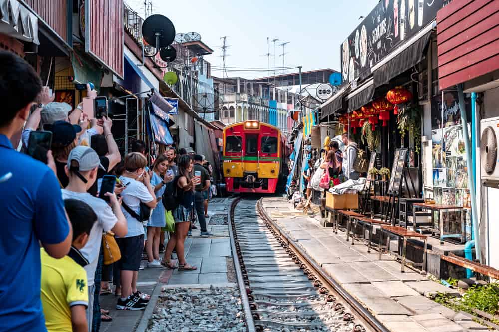 A train approaching at Maeklong Railway with people and shops at the sides in Bangkok, Thailand.