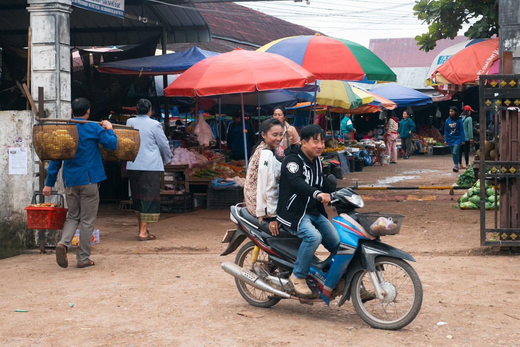 Two people riding a motorcycle at a market in Luang Namtha, Laos.