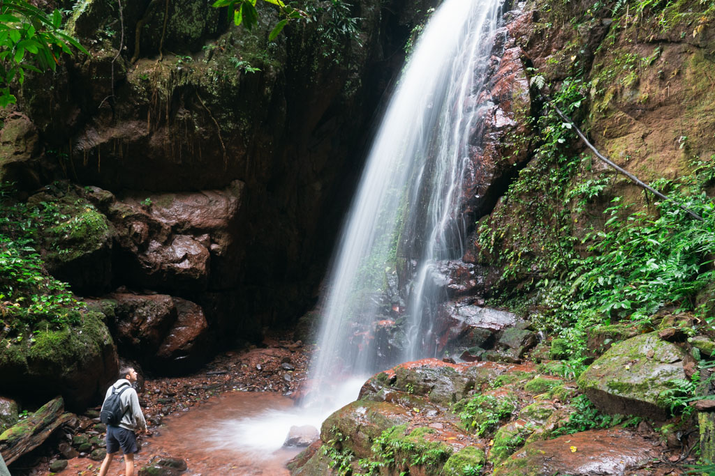 A person with a backpack standing in front of a waterfall in Luang Namtha, Laos.