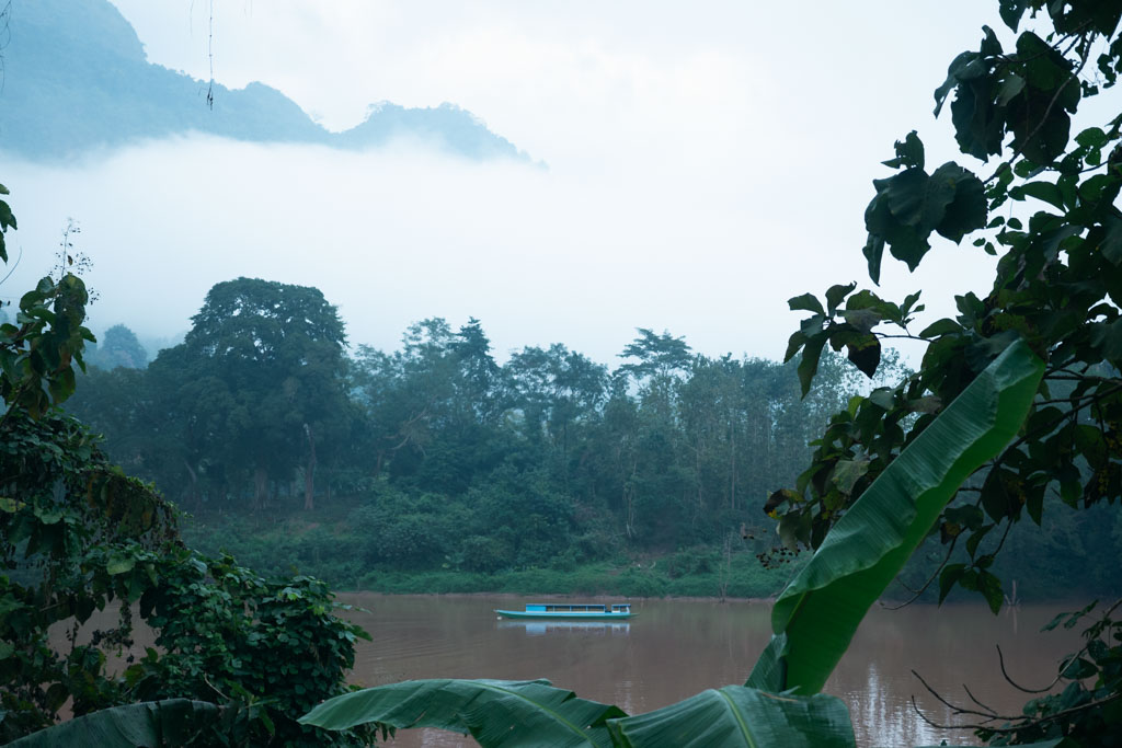 A cloudy forest in Laos with a boat on a river.