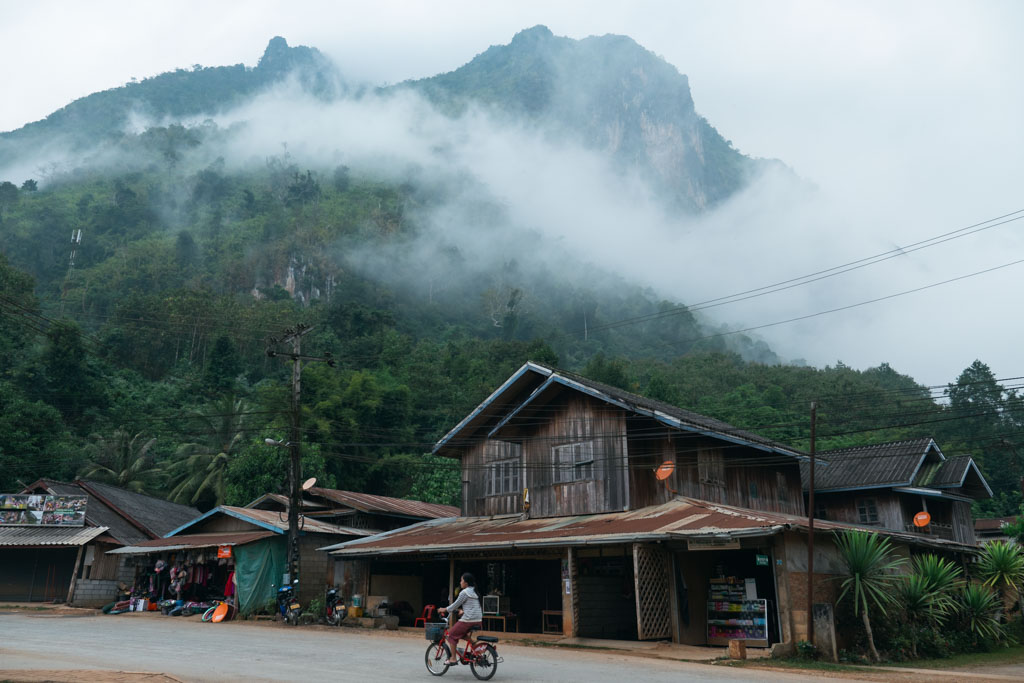 A misty mountain town in Laos with paved road and houses.