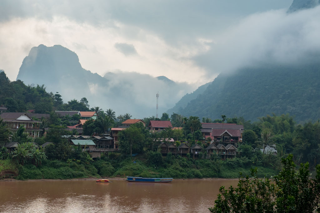 A cloudy and mountainous town in Laos with houses and a river.