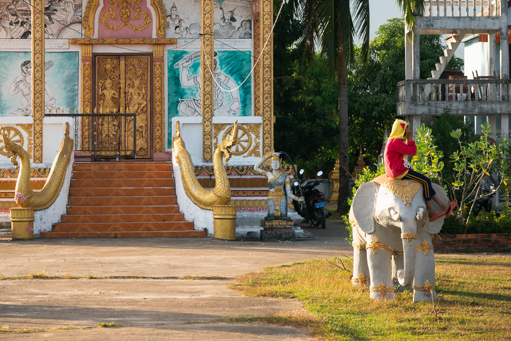A person sitting on an elephant statue in front of a temple in Laos.