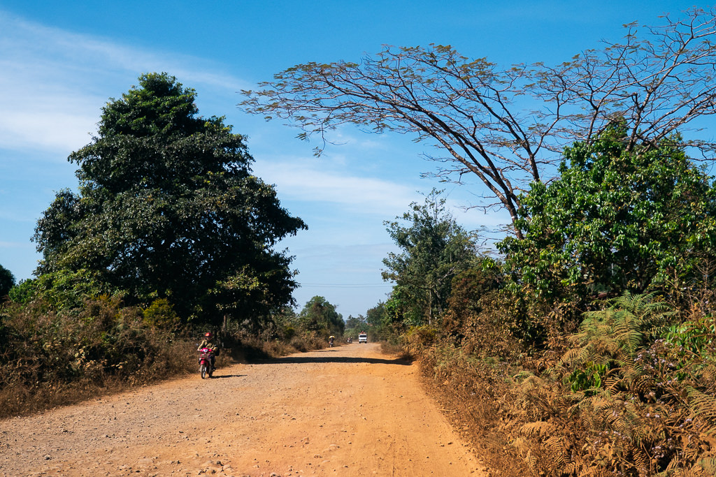 A person riding a motorcycle on an unpaved road in Laos.