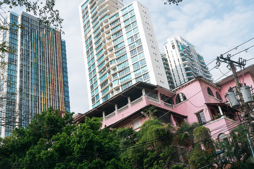 A low-angle view of a vibrant pink building with traditional architecture, nestled among green trees in Panama City.