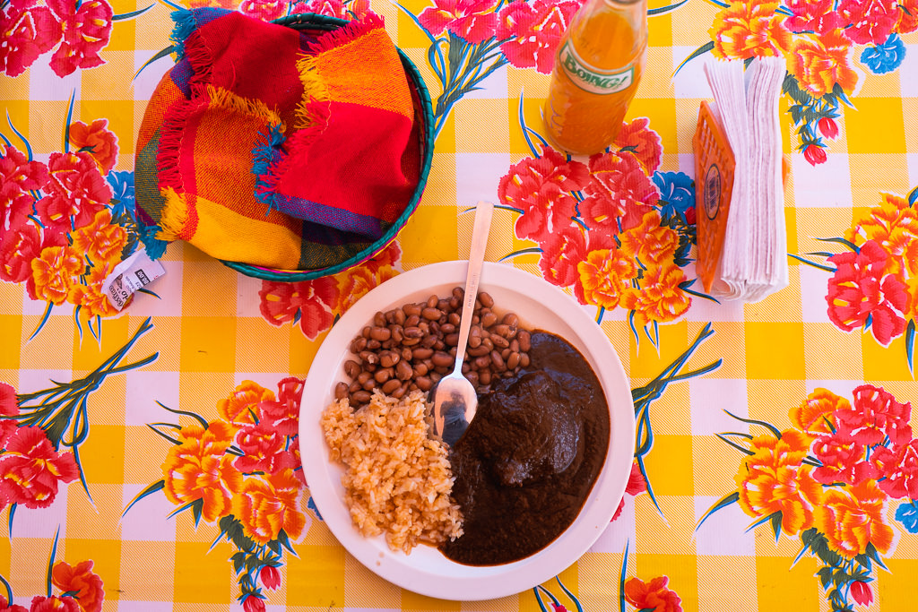 A plate of beans and other food, a bottle of drink, and tissues on a table with floral print.
