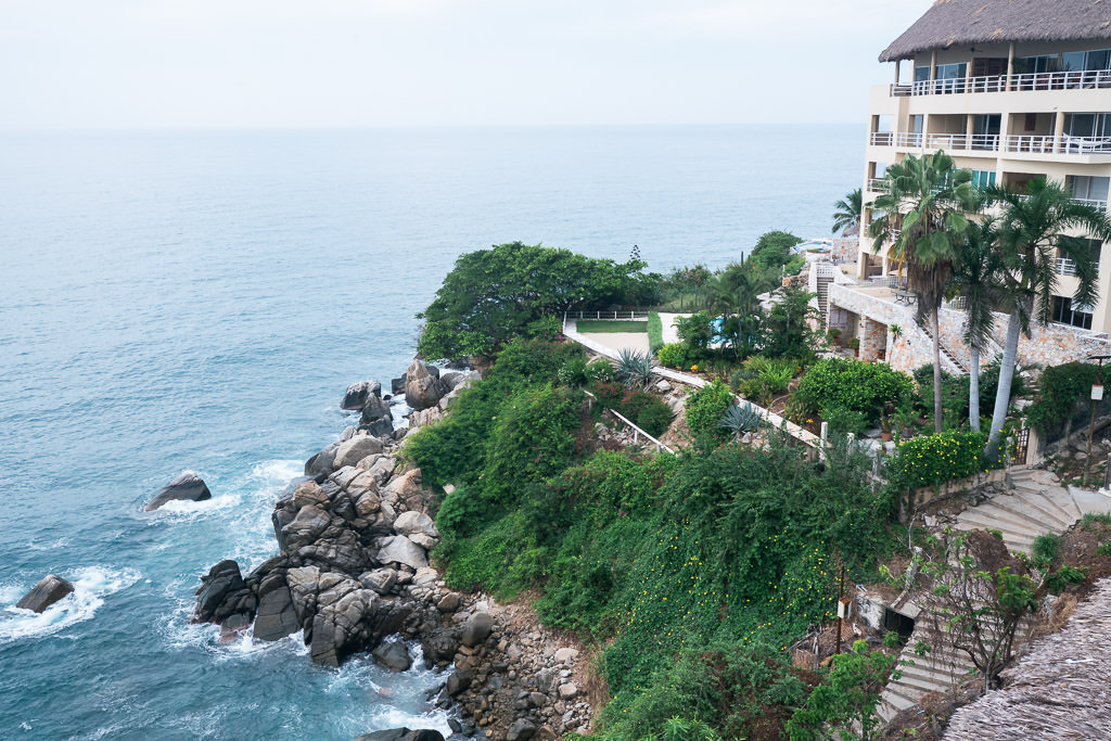 Coastal view of Rinconada, Mexico with a cliffside building overlooking the ocean, surrounded by lush greenery and rocky formations