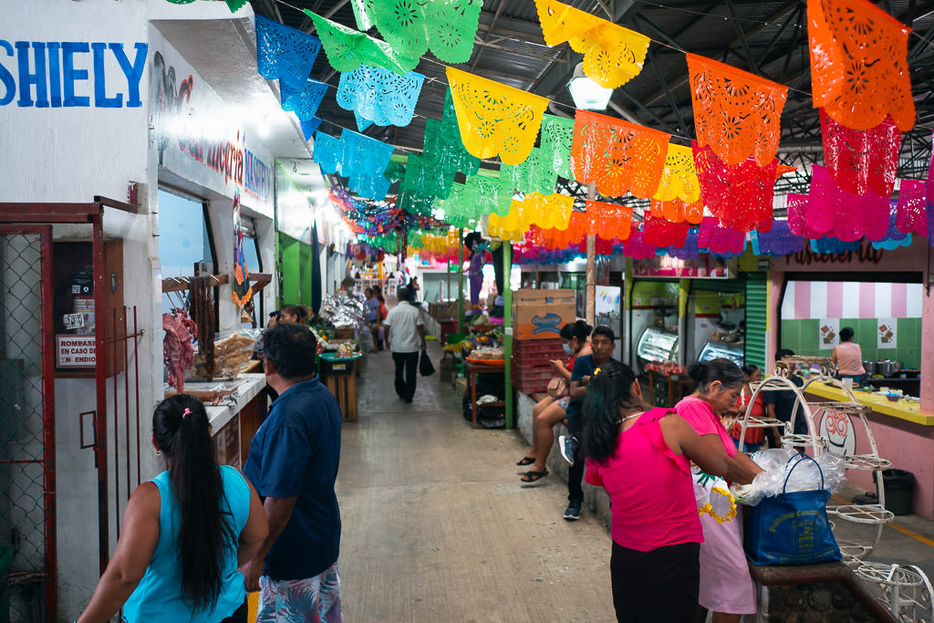 view of Mercado Benito Juárez in Puerto Escondido, Mexico showing colorful papel picado hanging overhead and people shopping