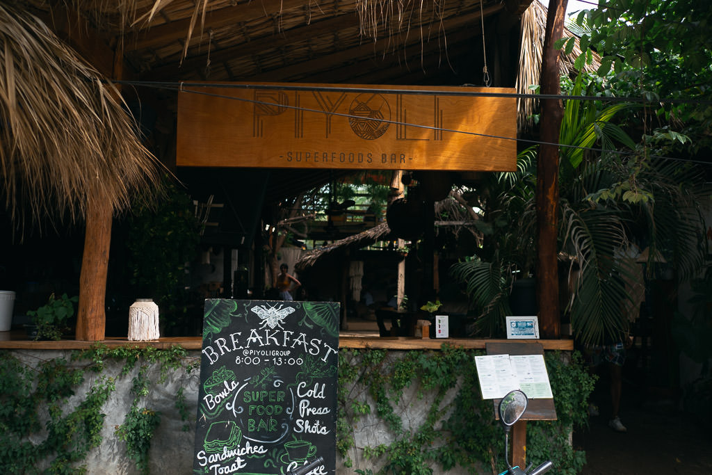 Outdoor view of Piyoli Superfoods Bar in La Punta, with a wooden sign and tropical decor