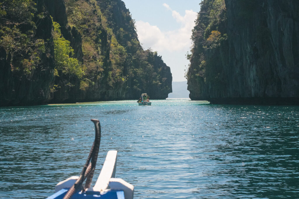 A boat's outrigger is visible in the foreground, with a view of El Nido in the background