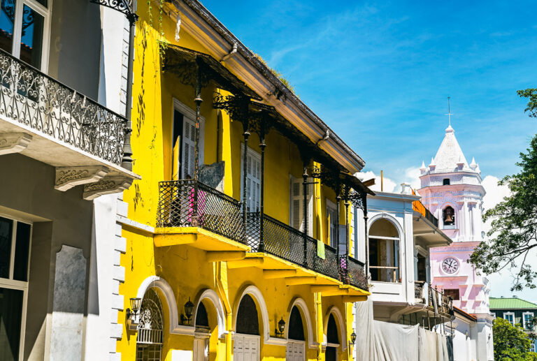 A yellow building with ornate balconies, set against a backdrop featuring a historic bell tower, in Casco Viejo, Panama.