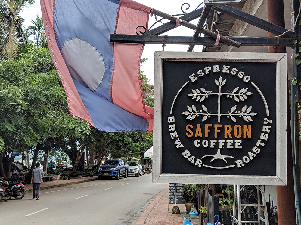 A Laos flag and a sign that says "Saffron Coffee" displayed on a sidewalk.