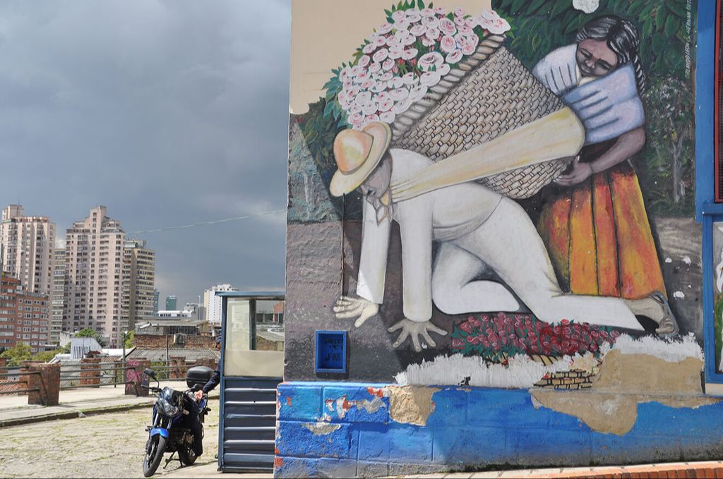 A street art in Bogota Colombia illustrating a woman assisting a man crawling with a basket of flowers on his back.
