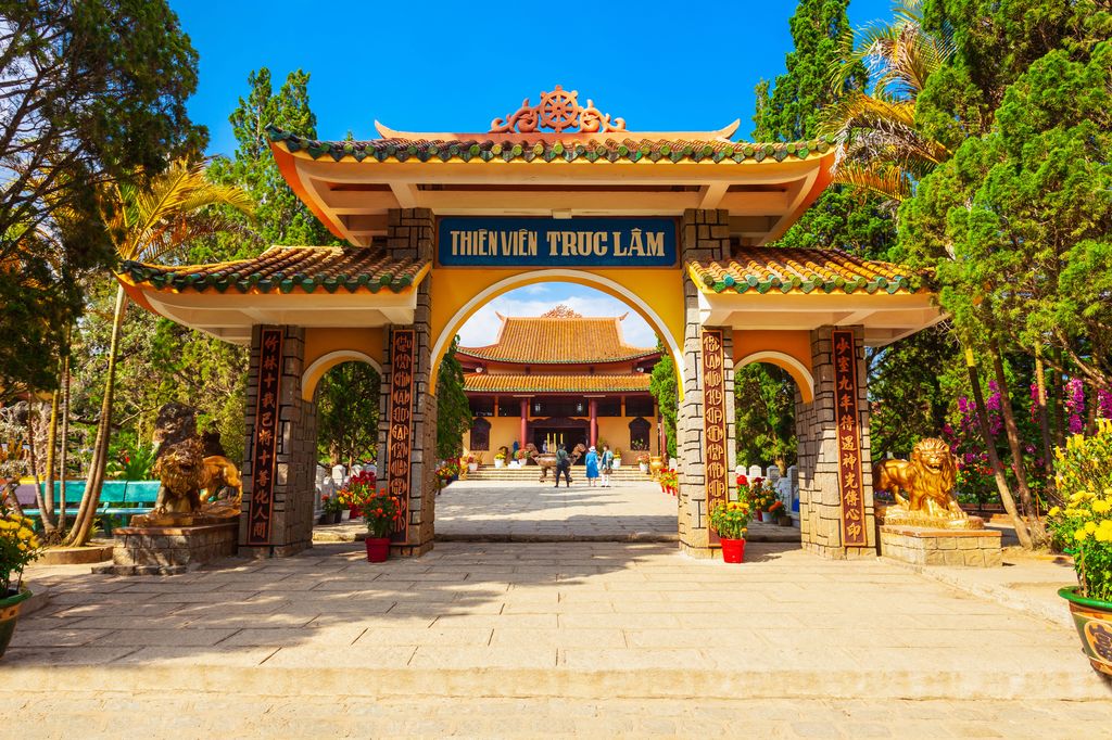 The yellow arch gate of Truc Lam Temple in Dalat, Vietnam surrounded by trees.