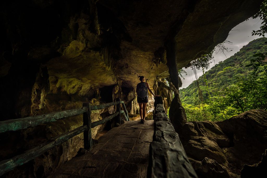 A woman standing backwards at a Cave in Cat Ba, Vietnam with a beautiful view of hills in the background.