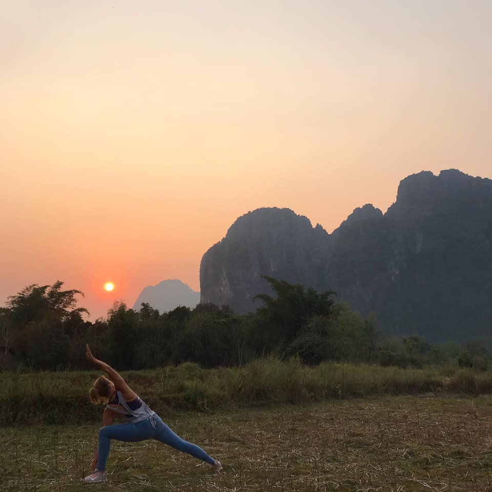 A woman doing sunrise yoga surrounded by mountains in Vang Vieng, Laos.